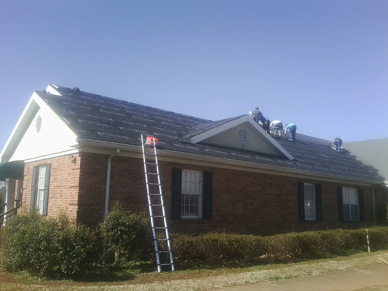 Crew tearing shingles off a brick ranch roof with a ladder set — Emergency Roof Repair work by our crew in New Richmond