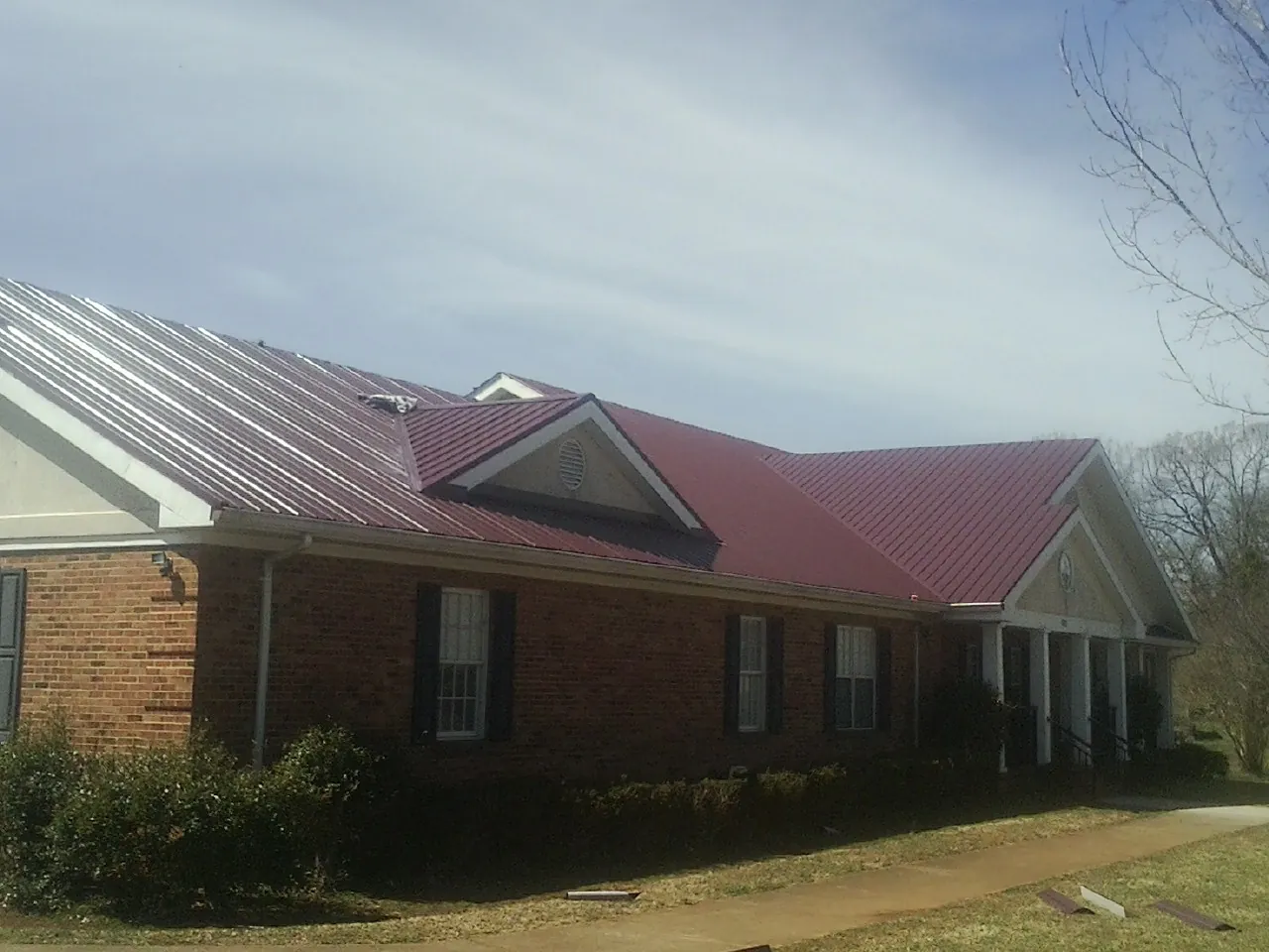Red metal roof with gabled entries on a long brick building, from a Hail Damage Roof Repair job in New Richmond