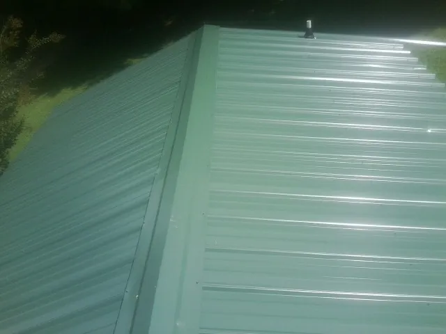 New green metal panels meeting at the ridge of a roof — Flat Roof Repair work by our crew in New Richmond